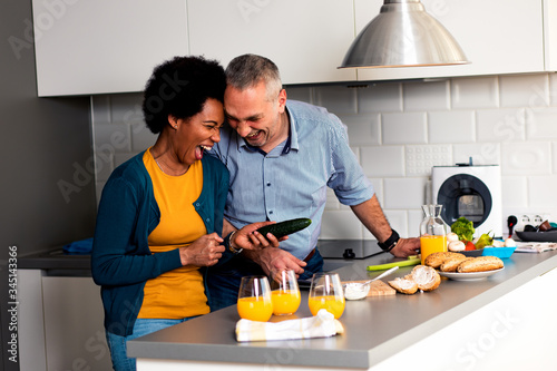 Smiling mixed race couple standing in the kitchen preparing sandwich for breakfast at home.