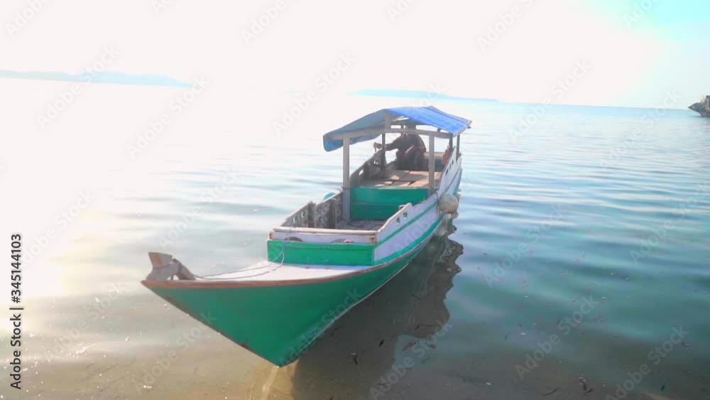 Man sitting in boat on shore at beach during sunny day, he is sailing nautical vessel - Lombok, Bali Man sitting in boat on shore at beach during sunny day, he is sailing nautical vessel - Lombok, Bali