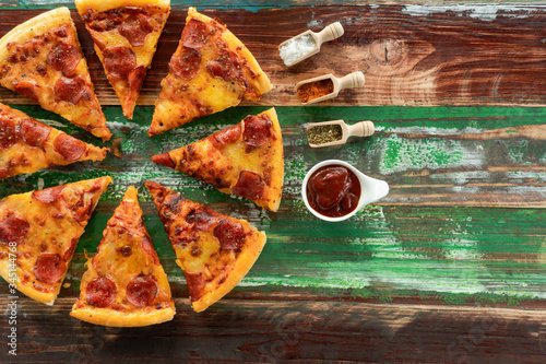 Top view of tasty pepperoni pizza, Sauce, Spices and Ingredients on the Wooden Spoon on colorful wooden table background. Copy space for text. Flat lay.