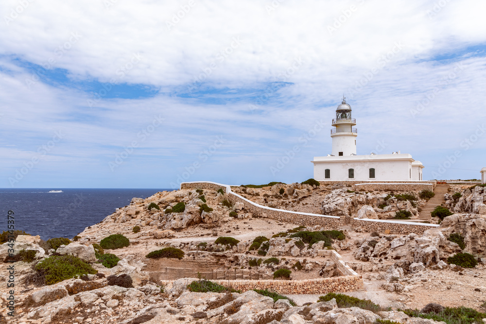 Beautiful seascape with a lighthouse (Faro de Cavalleria) on a cliff and a cruise ship in the sea. Menorca, Balearic islands, Spain
