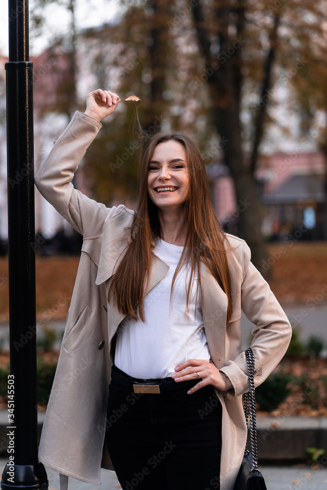 Outdoor fashion portrait of stylish young woman having fun, emotional face , laughing, Urban city street style wearing dark casual trousers, white sweater,creamy coat. and sunglasses Fashion concept.