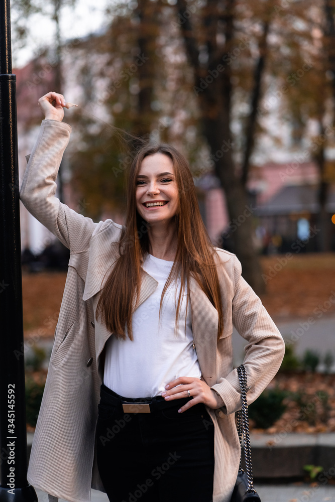 Outdoor fashion portrait of stylish young woman having fun, emotional face , laughing, Urban city street style wearing dark casual trousers, white sweater,creamy coat. and sunglasses Fashion concept.