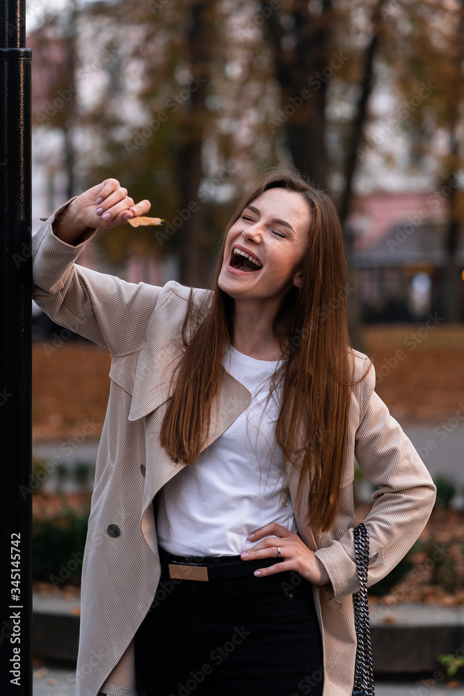 Outdoor fashion portrait of stylish young woman having fun, emotional face , laughing, Urban city street style wearing dark casual trousers, white sweater,creamy coat. and sunglasses Fashion concept.