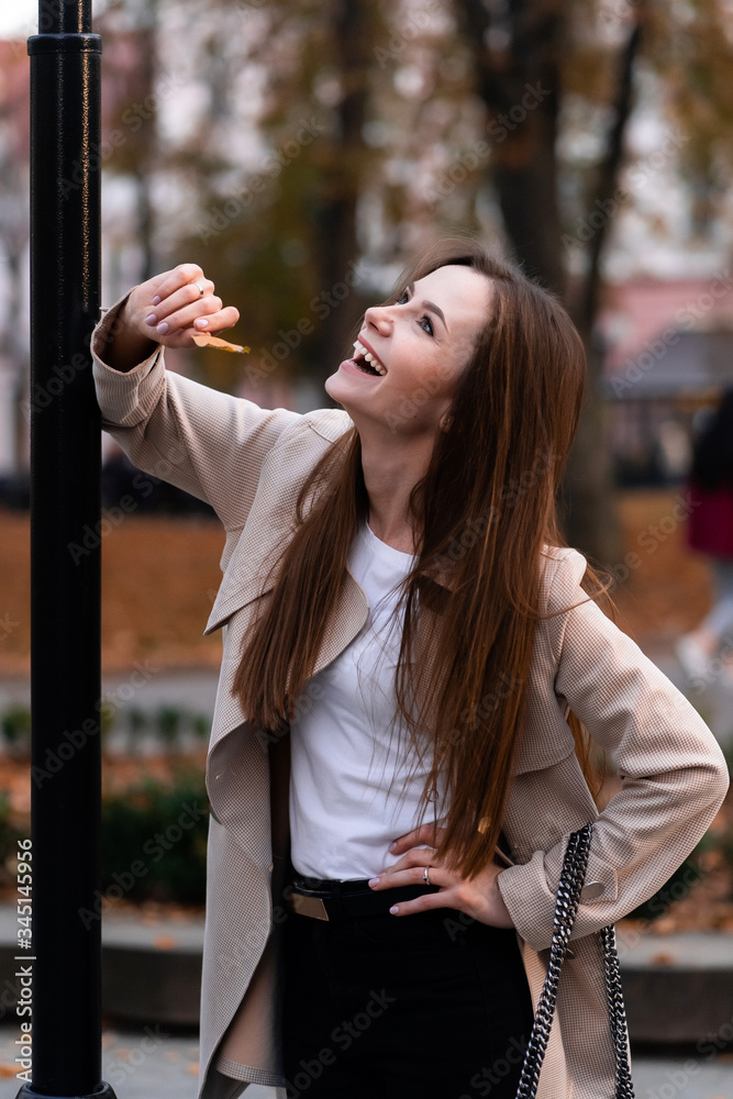 Outdoor fashion portrait of stylish young woman having fun, emotional face , laughing, Urban city street style wearing dark casual trousers, white sweater,creamy coat. and sunglasses Fashion concept.