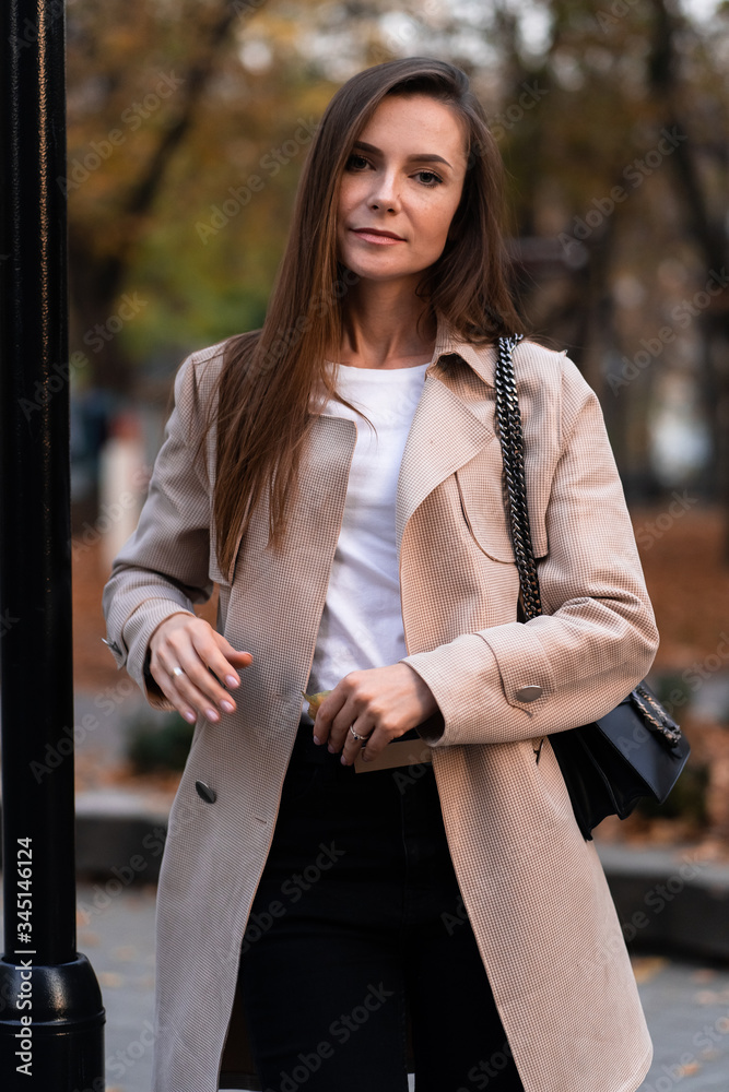 Outdoor fashion portrait of stylish young woman having fun, emotional face , laughing, Urban city street style wearing dark casual trousers, white sweater,creamy coat. and sunglasses Fashion concept.