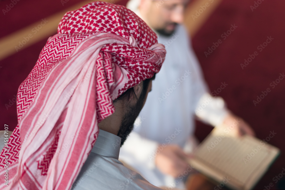 Two muliethnic religious muslim young people  praying and reading Koran together. Group of muslims praying in the mosque.