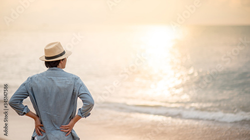 Asian man tourist wearing hat standing on tropical island beach enjoy looking at sunset. Relaxing holiday or vacation travel in summer season. Summertime trip concept © zephyr_p