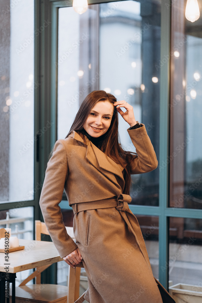 Outdoor fashion portrait of stylish young woman having fun, emotional face , laughing, Urban city street style wearing dark casual trousers, white sweater,creamy coat. and sunglasses Fashion concept.