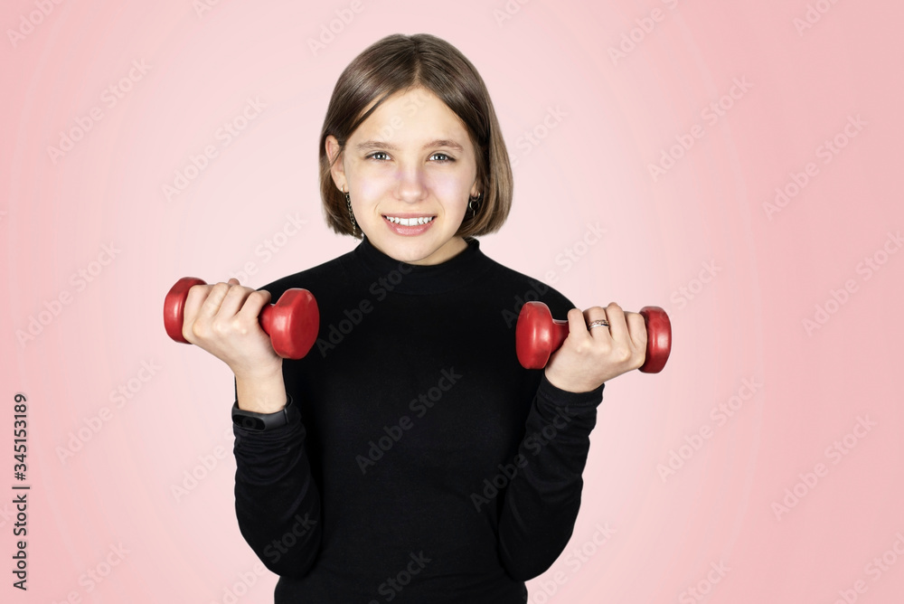 Teenage girl holds red light dumbbells in her hands and makes morning exercise after yoga on a pink background and smiles. Gender diversity in sports photo Teenage girl holds red light dumbbells in her hands and makes morning exercise after yoga on a pink background and smiles. Gender diversity in sports photo