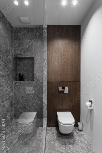 Bathroom in grey tones  stylish in modern design  dark wooden tumble  glass and mirror. Chrome crane. Black towel