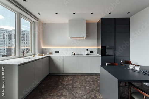 bright kitchen with dark table, convenient location of kitchen accessories and equipment, modern style, White walls, marble working surface and parquet floor. There s a glass of milk on the table and