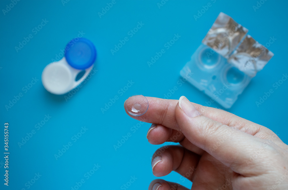 Сontact lenses, blisters and container on a blue background. Hands with a contact lens.