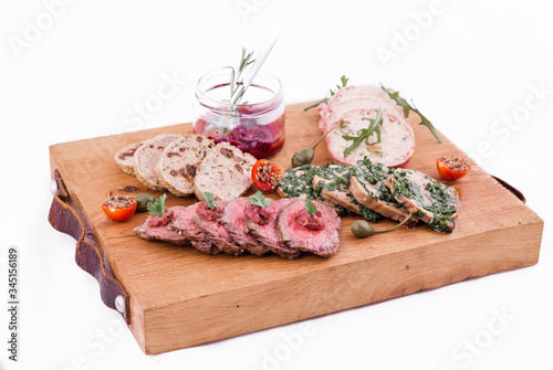 On a wooden plate, beef roast beef, herb marinated tongue, chicken terrine, duck galantin, cherry sauce photo