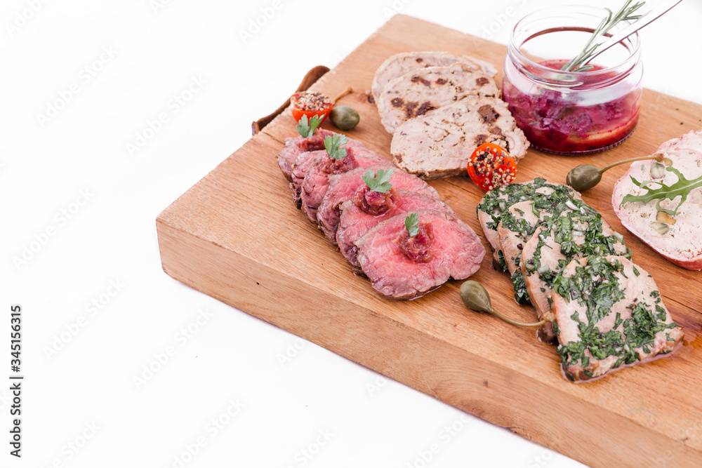 On a wooden plate, beef roast beef, herb marinated tongue, chicken terrine, duck galantin, cherry sauce On a wooden plate, beef roast beef, herb marinated tongue, chicken terrine, duck galantin, cherry sauce