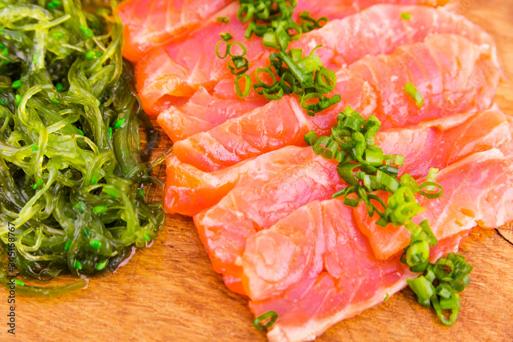 Fish platter on a wooden board. Lightly salted salmon, chuka salad and green onion decor Fish platter on a wooden board. Lightly salted salmon, chuka salad and green onion decor