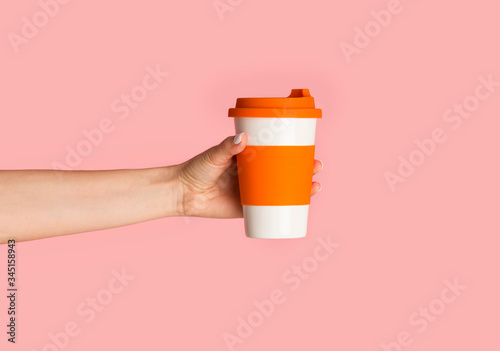 Millennial girl holding reusable eco cup with hot beverage on pink background, close up photo