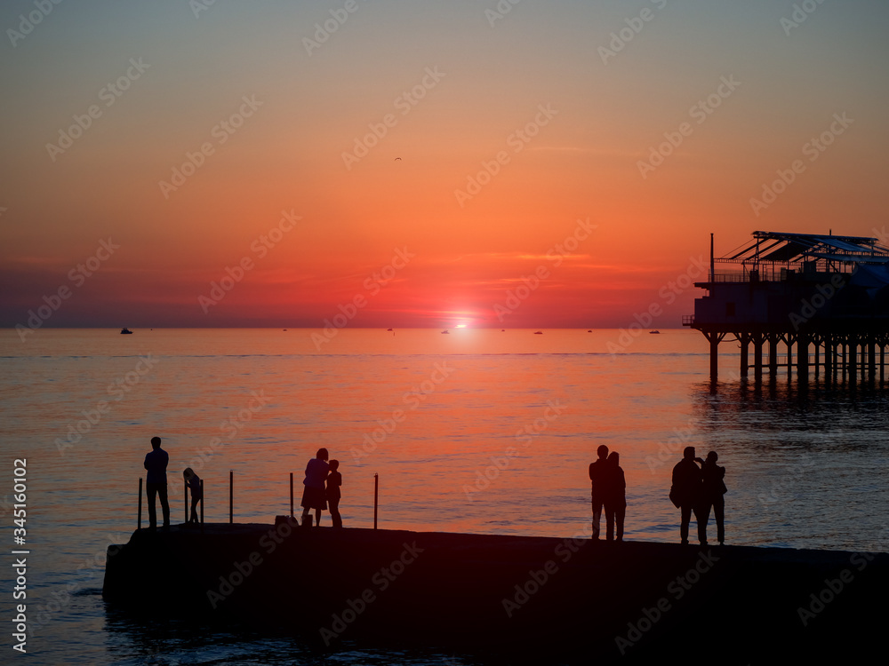 Silhouettes of people on the pier against the backdrop of the sea sunset