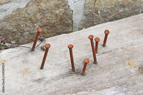 Seven rusty nails, nailed into a railway sleeper, against a background of masonry