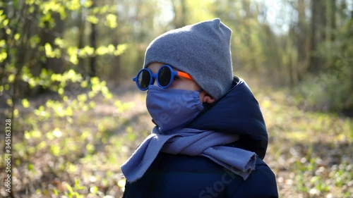boy walks in a mask protected from the virus and colorful round glasses in the forest during the coronavirus epidemic