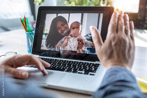 Man waving and speaking on video call with his wife and baby daughter on laptop in the office.