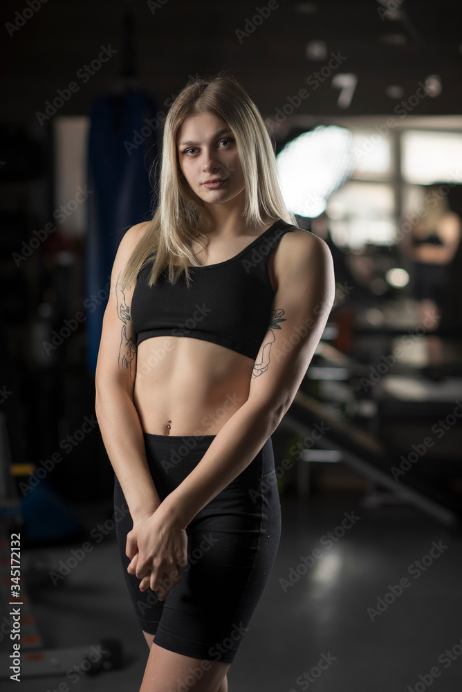 Portrait of a young girl, a fitness trainer in a dark sports uniform with a gym.