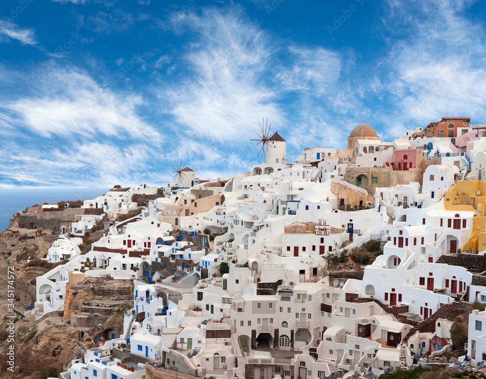 Panoramic view of Oia town at sunset, Santorini island, Cyclades, Greece. Traditional famous white houses, windmills and churches over the Caldera in Aegean sea.