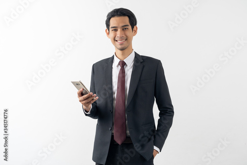 happy young asian businessman smiling and holding a smart phone in formal suit isolated on white background.