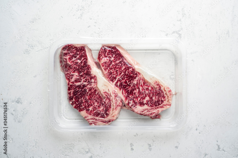 Raw Wagyu steak of marbled beef in vacuum packaging on a white stone background