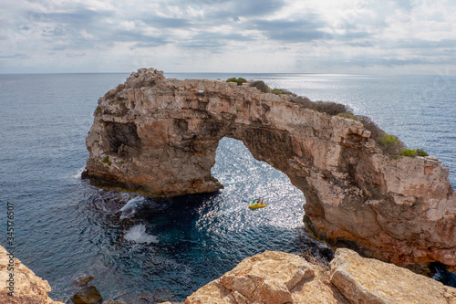 Es Pontas arc ("The big bridge") in the Mediterranean sea, Mallorca island, and people in the yellow boat under the arc.