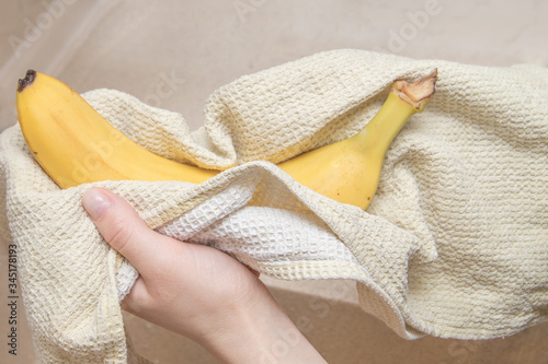 Women's hands wipe a banana with a towel, against the background of a fruit basket. Hygiene. Stay home. Quarantine. Pandemic Coronavirus.