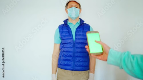 courier in uniform face mask reaching out hand with paper packages or bags on white background. takeout meal, deivery to home, food delivery, shopping order online. customer accepts food delivery photo