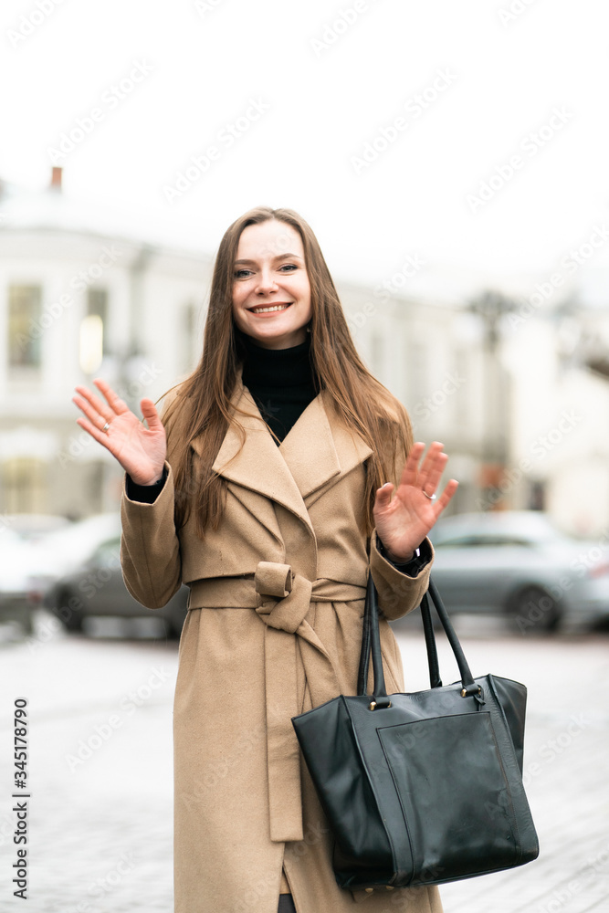 Outdoor fashion portrait of stylish young woman having fun, emotional face , laughing, Urban city street style wearing dark casual trousers, white sweater,creamy coat. and sunglasses Fashion concept.