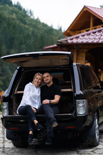 Portrait of beautiful sexy blonde woman and man sitting in luxury dark car . Fashion and business concept. Idea for couple photoshoot with car. Valentines day, surprise. © MONIUK ANDRII