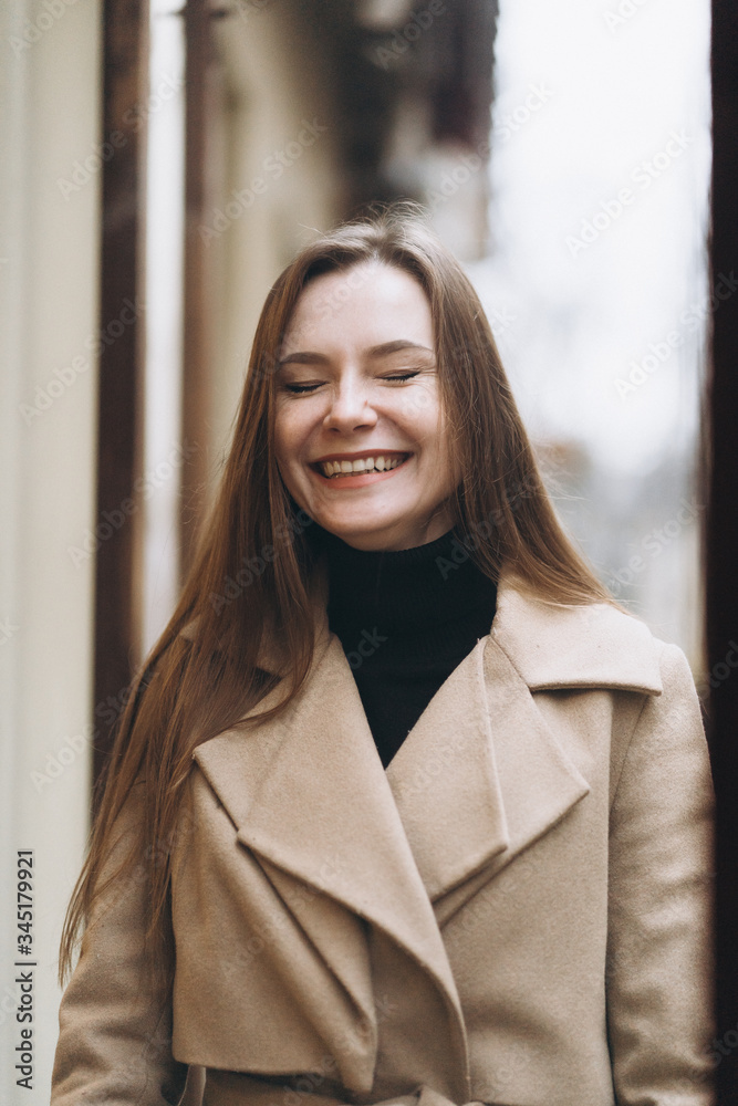 Outdoor fashion portrait of stylish young woman having fun, emotional face , laughing, Urban city street style wearing dark casual trousers, white sweater,creamy coat. and sunglasses Fashion concept.
