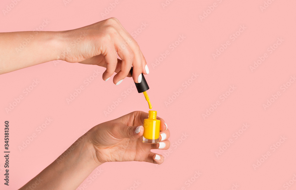 Close up of nail artist holding bottle of yellow enamel on pink background, copy space Close up of nail artist holding bottle of yellow enamel on pink background, copy space