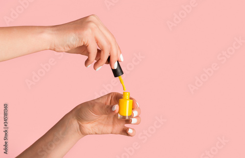 Close up of nail artist holding bottle of yellow enamel on pink background, copy space