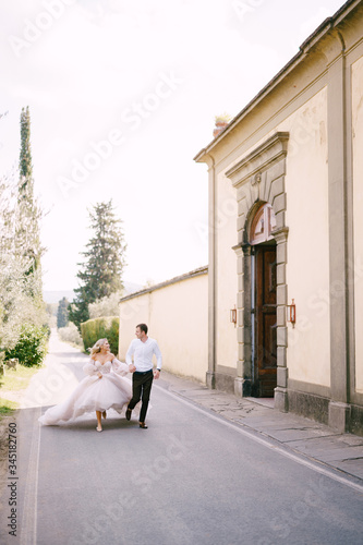 Beautiful bride and groom running hand in hand outside of old villa in Italy, in Tuscany, near Florence. © Nadtochiy