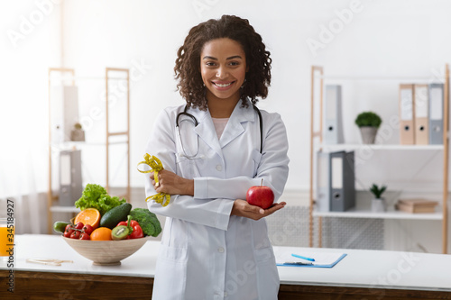 African dietician with crossed arms holding fresh apple photo