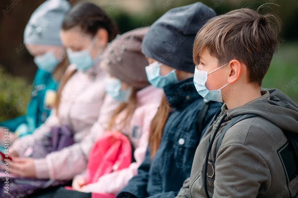 School-age children in medical masks sit on a bench.