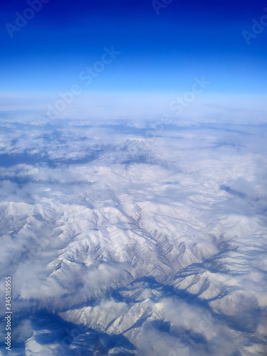 Vertical photography of snowy Zagros mountains in Iran made through window during flight on airplane. Aerial view. Selective focus. Clear blue sky above horizon. Beautiful landscape.