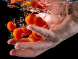 Hand holding fresh tomatoes falling into water with splash. Closeup of fresh and health cherry tomatoes falling into clear water on black background Red tomato drop in water with bubble. Food concept