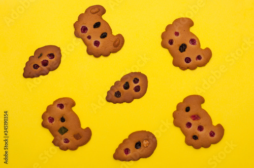 Top view of homemade cookies decorated with berries, raisins and colored candied fruits at yellow background
