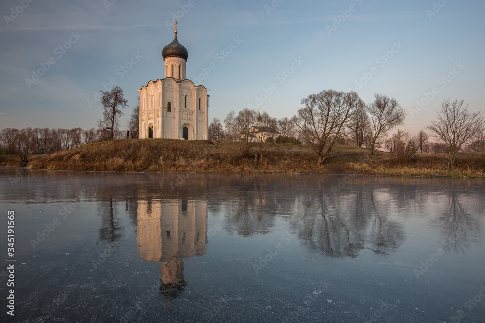 Obraz premium A beautiful temple on a background of bright golugobo sky stands on the shore of a lake is reflected in the ice at sunset