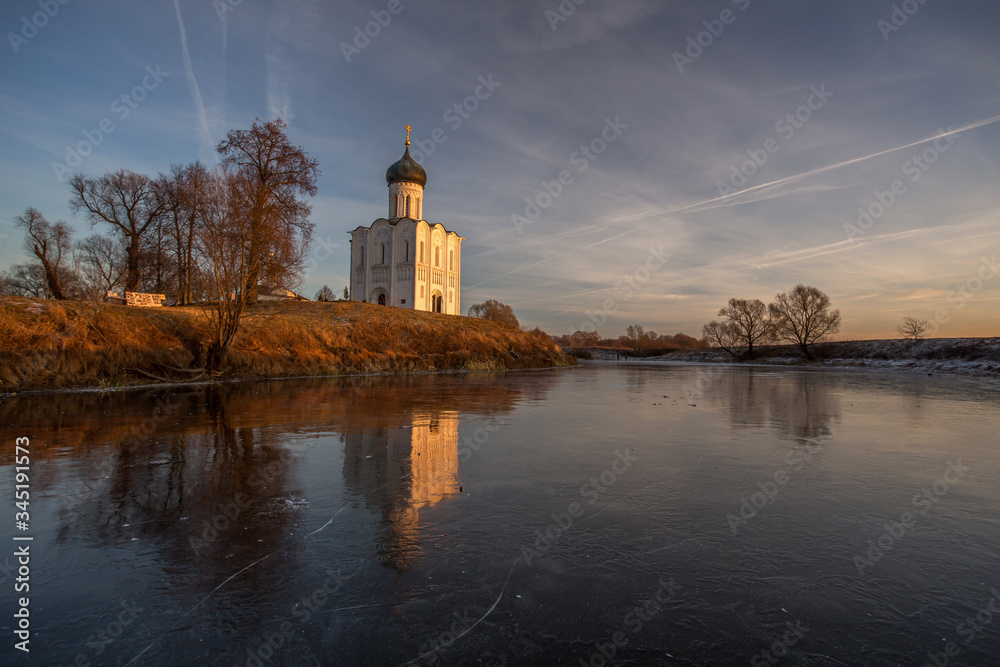 A beautiful temple on a background of bright golugobo sky stands on the shore of a lake is reflected in the ice at sunset