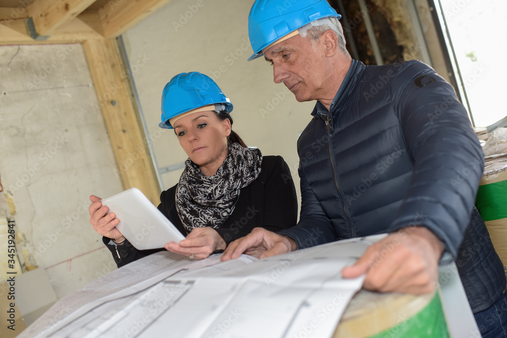 Architect checking his blue-print while hois assistante reds notes on his tablet. Architect checking his blue-print while hois assistante reds notes on his tablet.