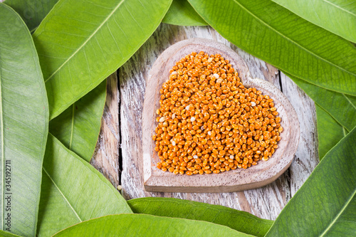 Bowl with red millet grains surrounded by green leaves on wooden background, top view photo