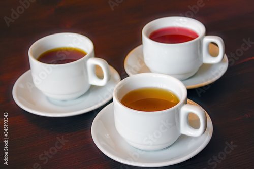 Three white porcelain cups with black, red and green tea on a wooden table background close-up.