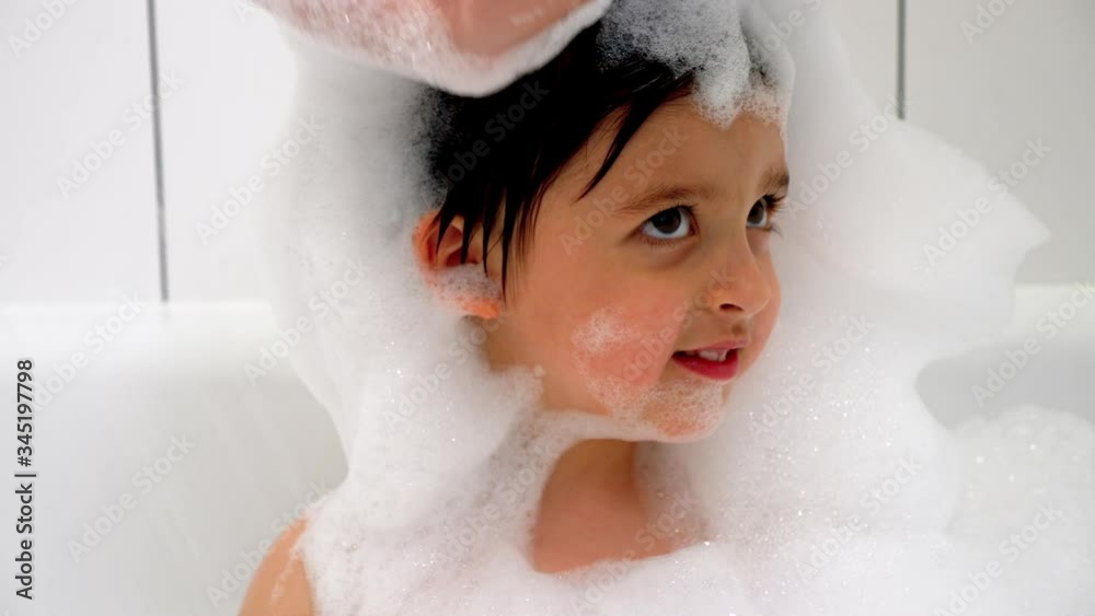 three year old boy with big eyes bathes in a white bathroom with black stripes with lots of foam mom puts foam on her head three year old boy with big eyes bathes in a white bathroom with black stripes with lots of foam mom puts foam on her head