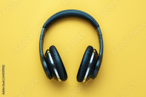 Photo of black stylish modern wireless headphone in neon lights over yellow background.