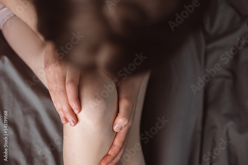 Top view cropped images of unrecognizable woman with knee pain, young woman massaging her painful knee sitting on bed at home, Health care concept. Selective focus